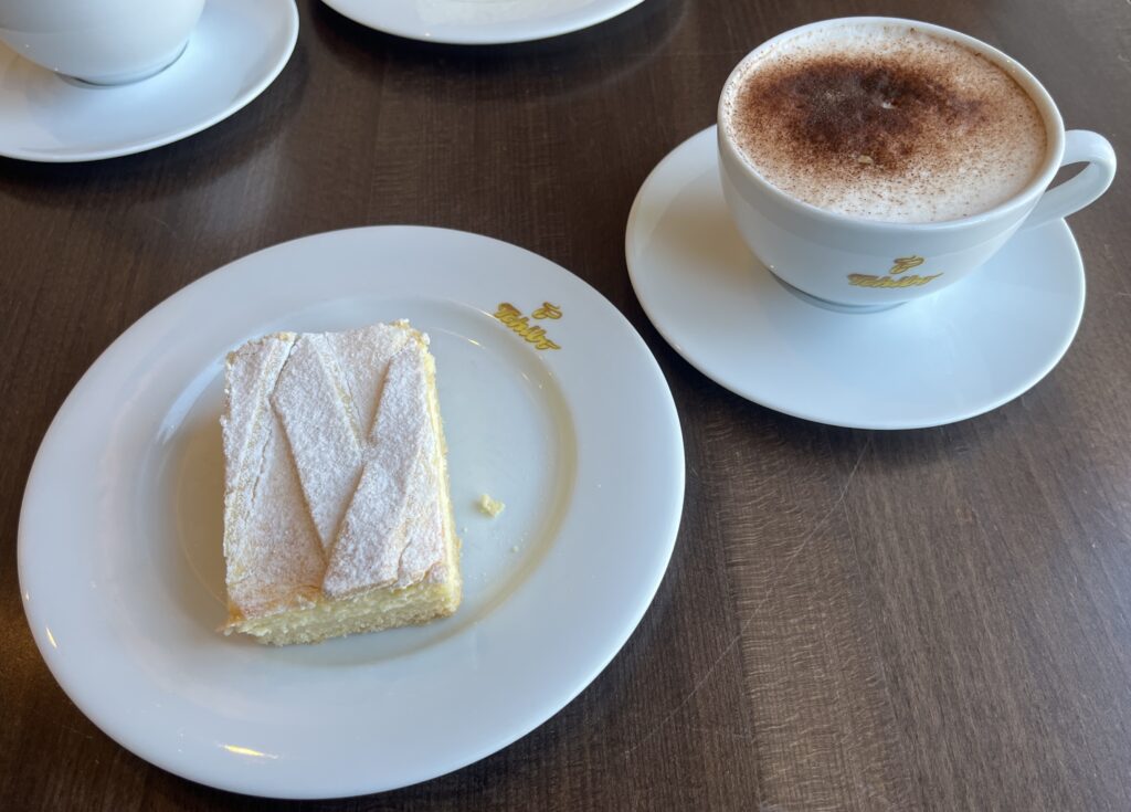 Das Bild zeigt einen Teller mit einem Stück Kuchen und eine Kaffeetasse